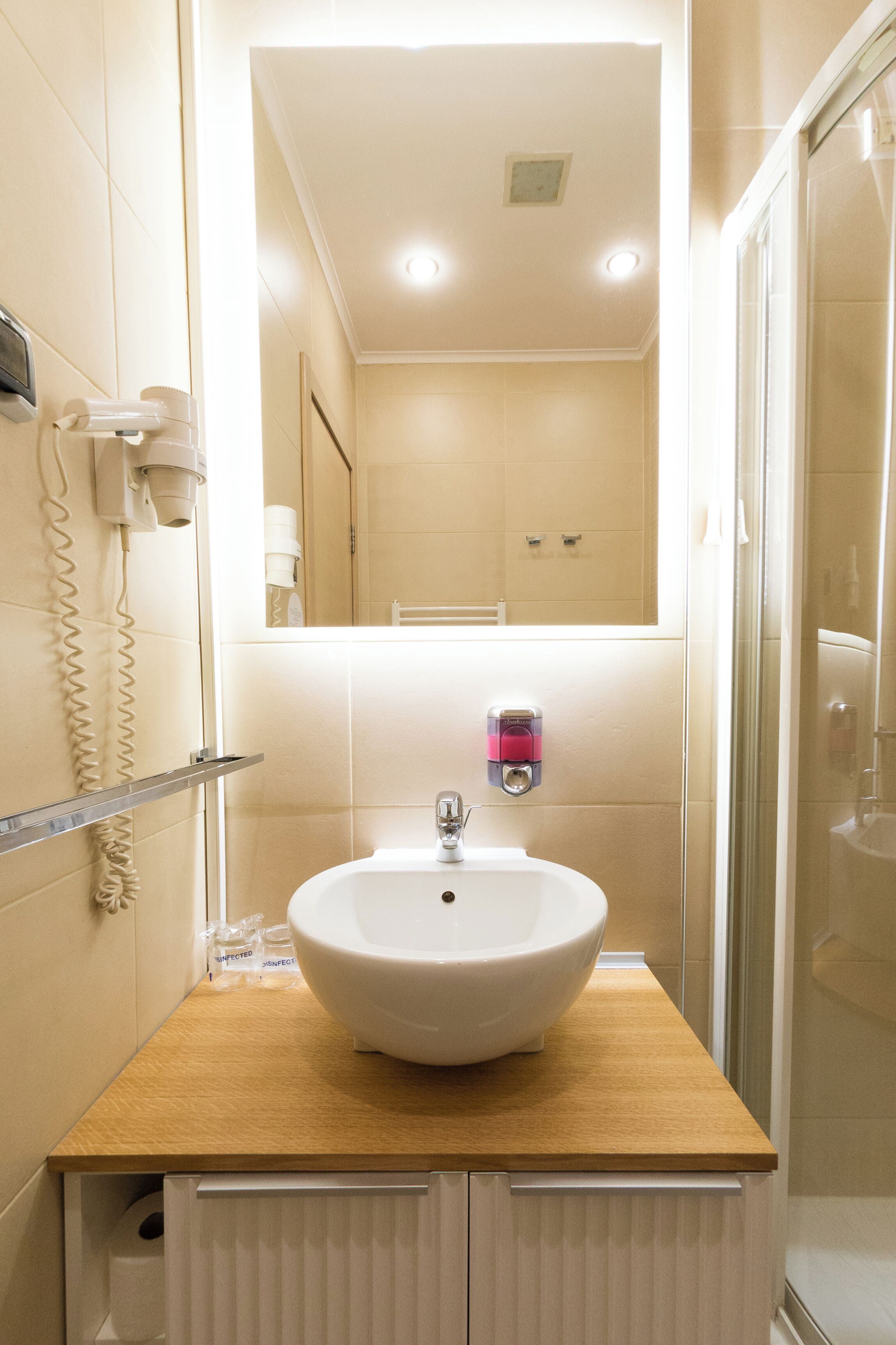 Un baño con lavamanos blanco, espejo, toallero y cabina de ducha de vidrio.