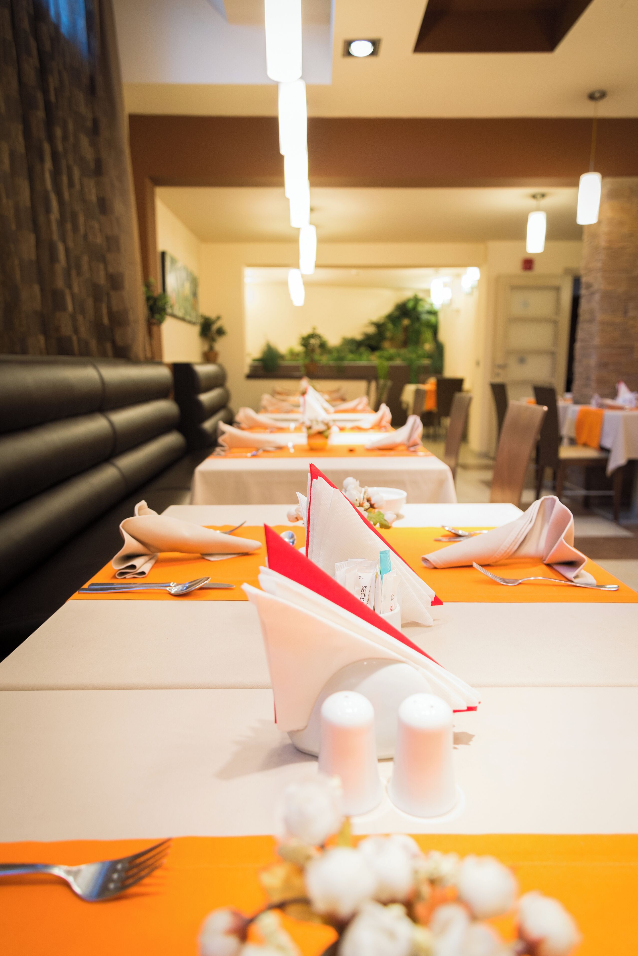 Ein Restaurant mit gedeckten Tischen, mit orangefarbenen Platzsets und ordentlich gefalteten Servietten.