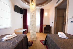 A hotel room with two beds, a desk, a chair, a TV, and a stone pillar.