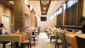 A restaurant with multiple tables, chairs, and a large stone pillar. - Vigor Hotel (Novi Sad)