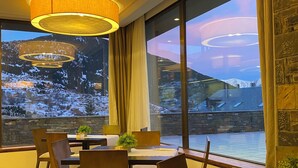 Un comedor con mesas y sillas, amplias ventanas con vistas a montañas nevadas e iluminación colgante moderna.