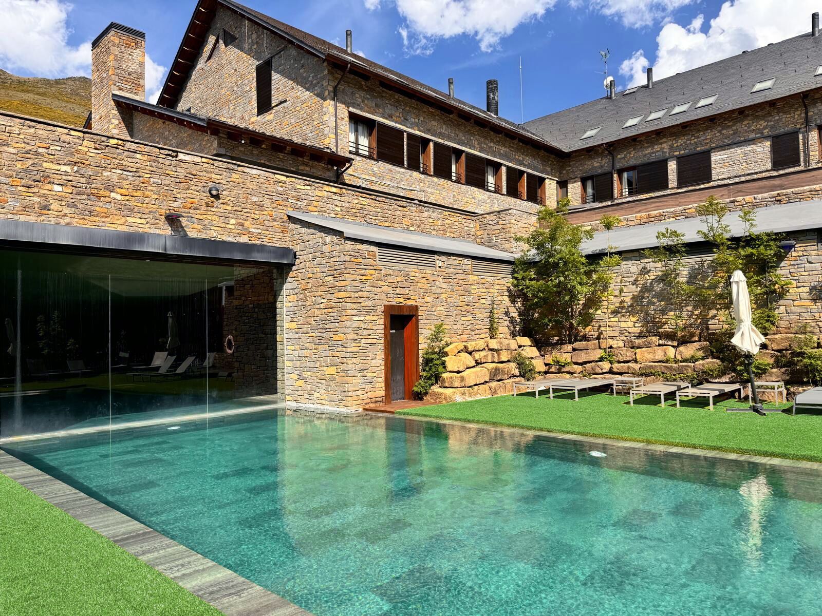 A stone building with a swimming pool, outdoor seating, and a covered area.