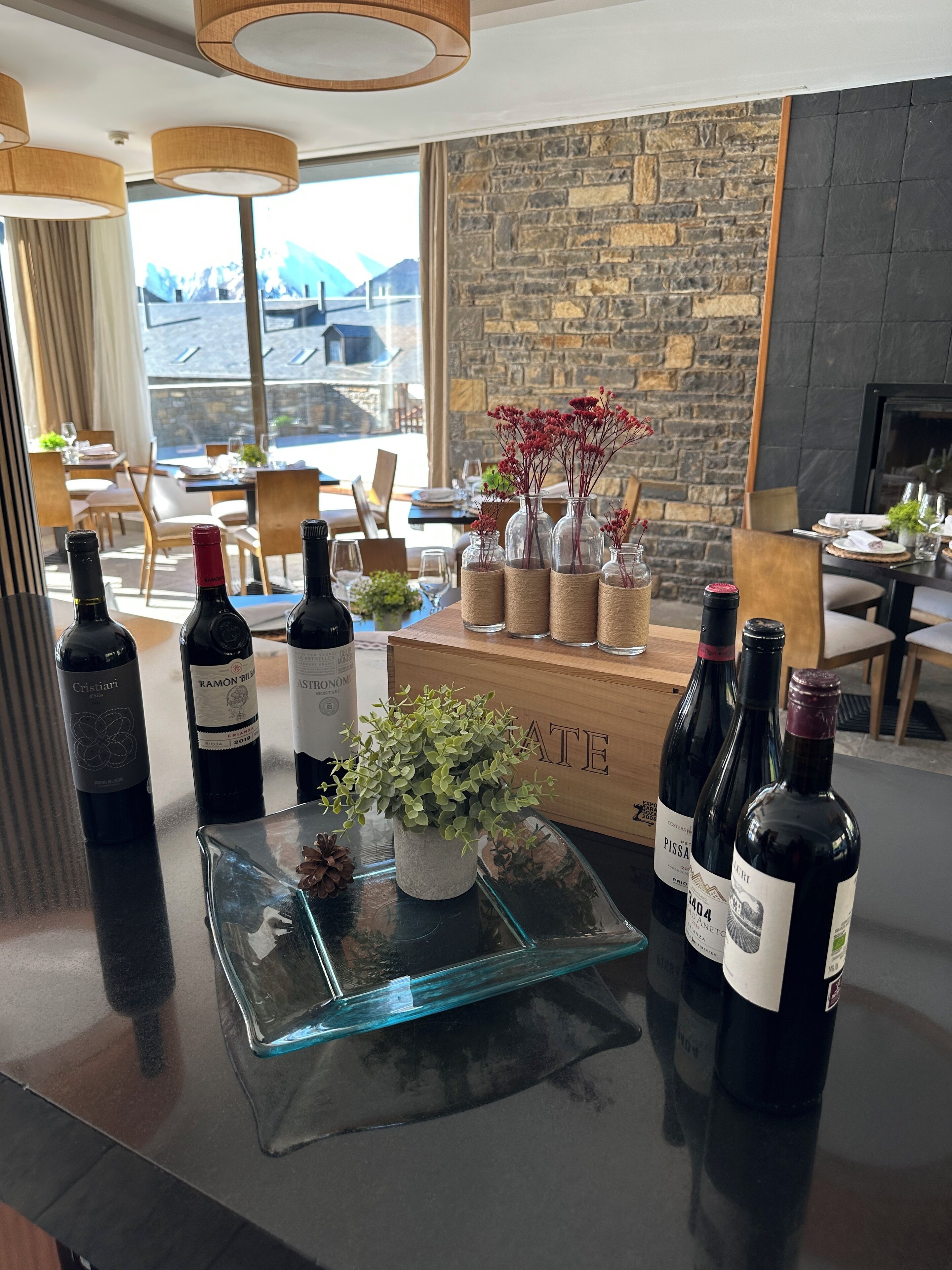 Un coin bar avec des bouteilles de vin, une plante en pot et un mur de pierre en arrière-plan.