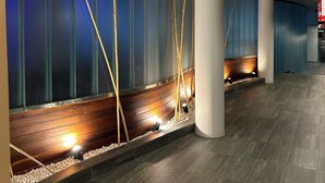Un moderno hall de entrada con una pared curva, un banco de madera y una pequeña fuente decorada con cañas de bambú.
