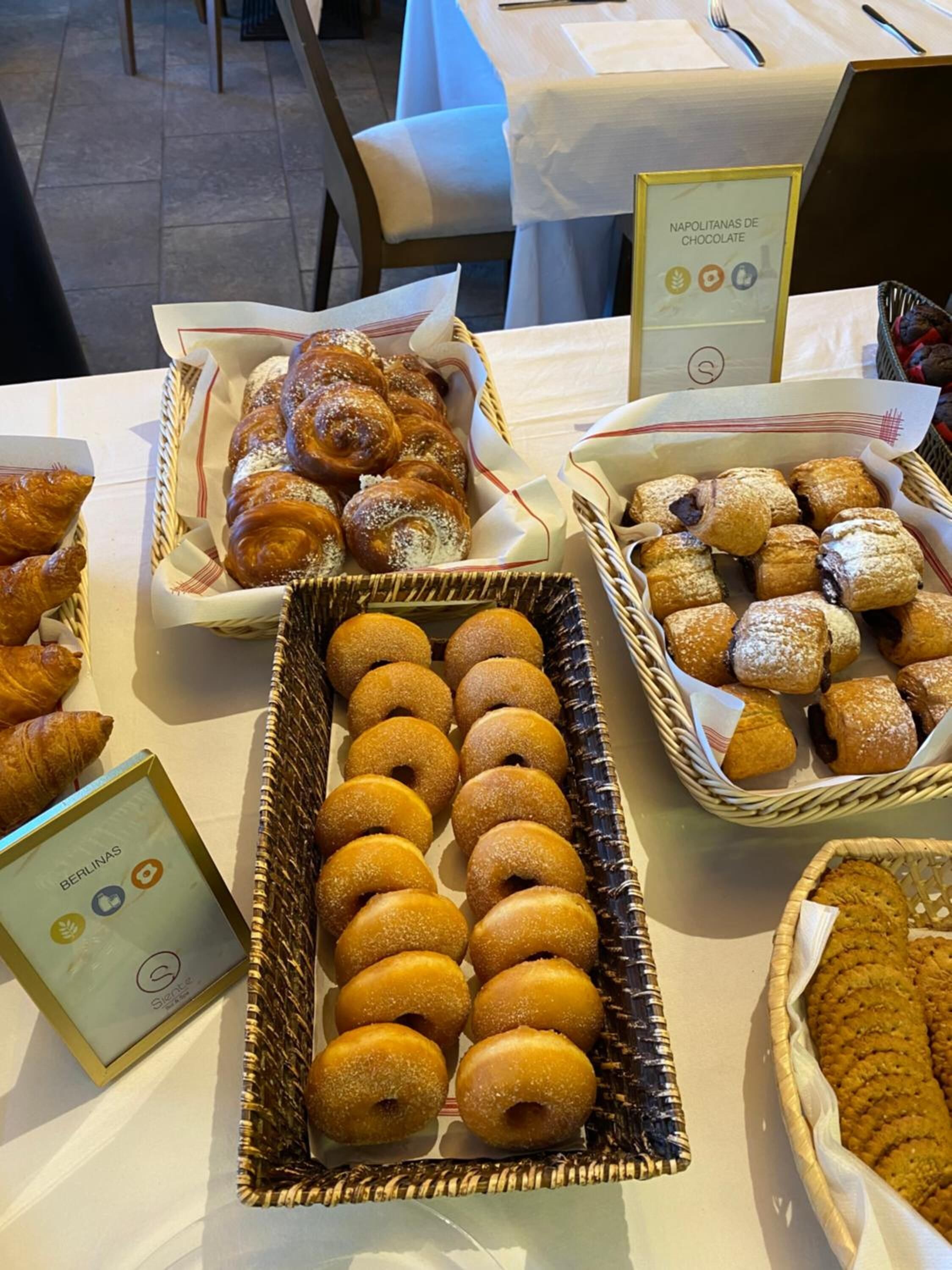 Una mesa con diversos productos horneados, como pasteles y donas, dispuestos en cestas y cajas.