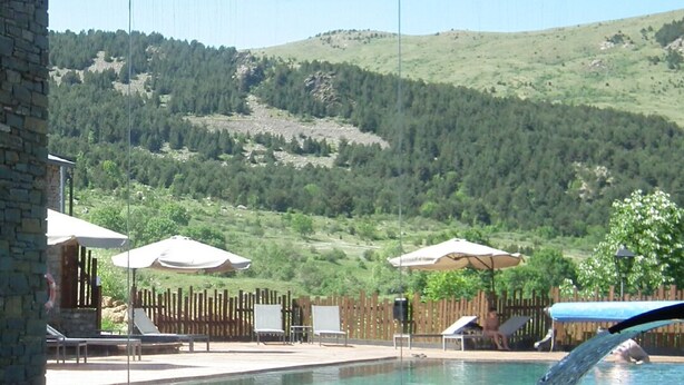 Una piscina con valla de madera y sillas de descanso, con colinas verdes y un cielo despejado de fondo.