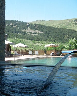 Une piscine entourée d’une clôture en bois et agrémentée de chaises longues, le tout se fondant dans un paysage de collines verdoyantes et d’un ciel dégagé.