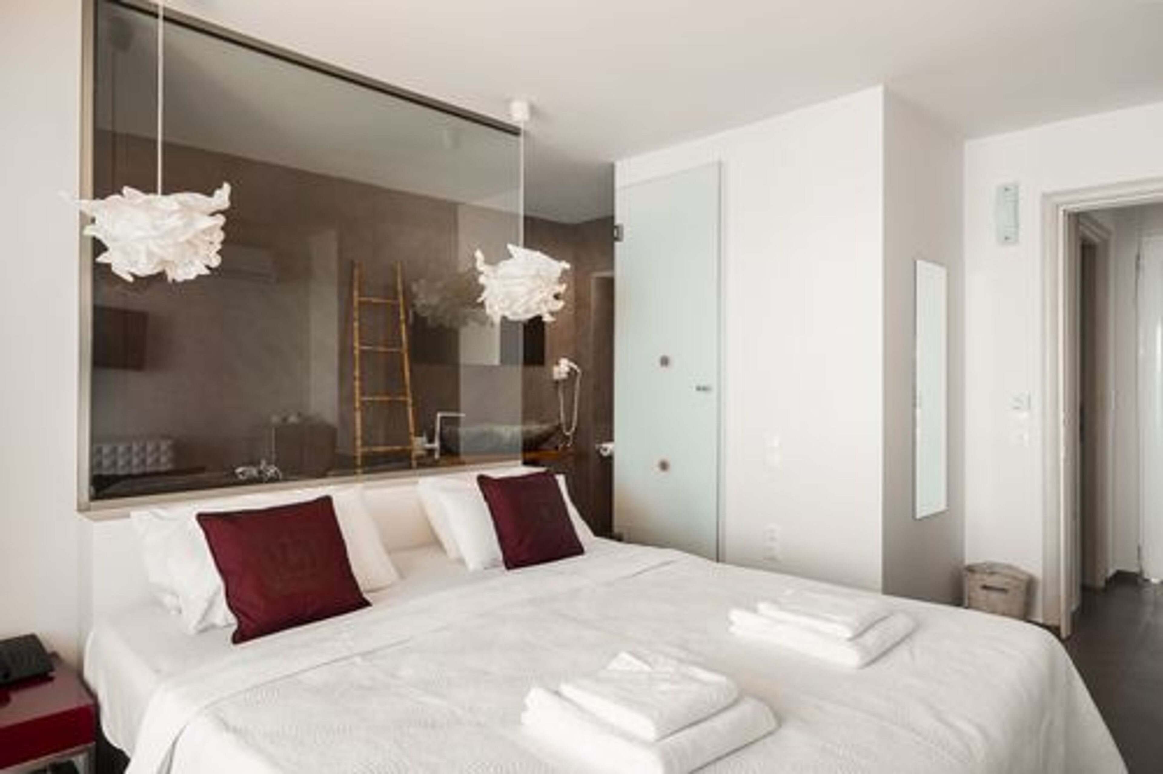 Een moderne hotelkamer met een groot bed, witte lakens en een grote spiegel die de kamer weerspiegelt.