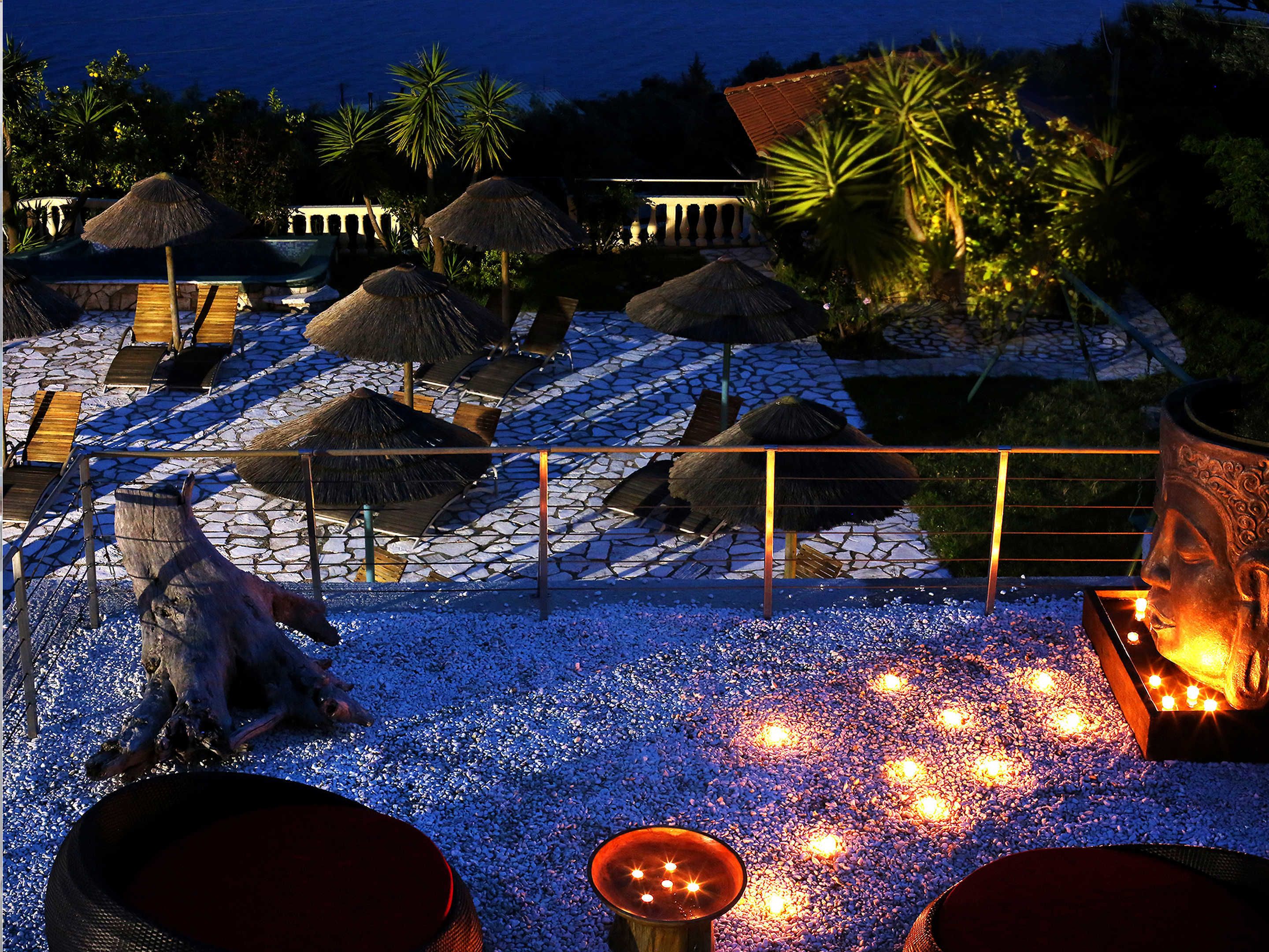 Area piscina di un resort di notte, con ombrelloni di paglia, poltroncine da relax e una statua decorativa a forma di cavallo.