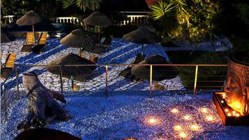 A nighttime resort pool area with thatched umbrellas, lounge chairs, and a decorative horse statue.