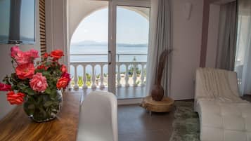 A room with a bathtub, a white sofa, a vase of flowers, and a view of the sea through a glass door.