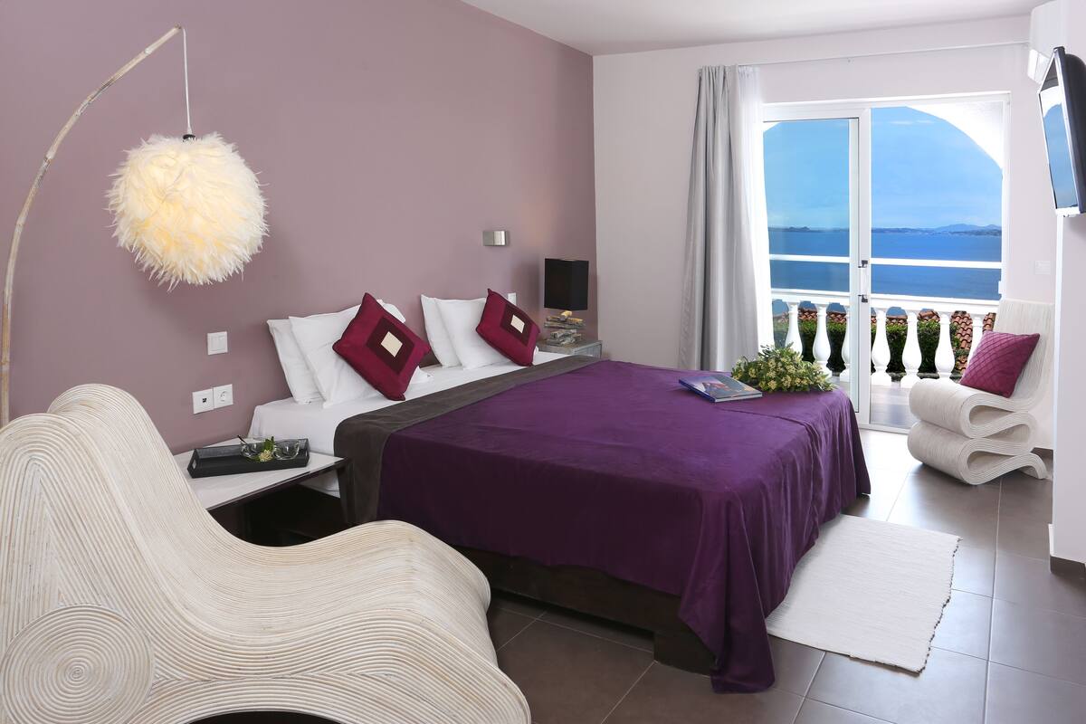 A modern bedroom with a large bed, a sitting area, and a view of the sea.