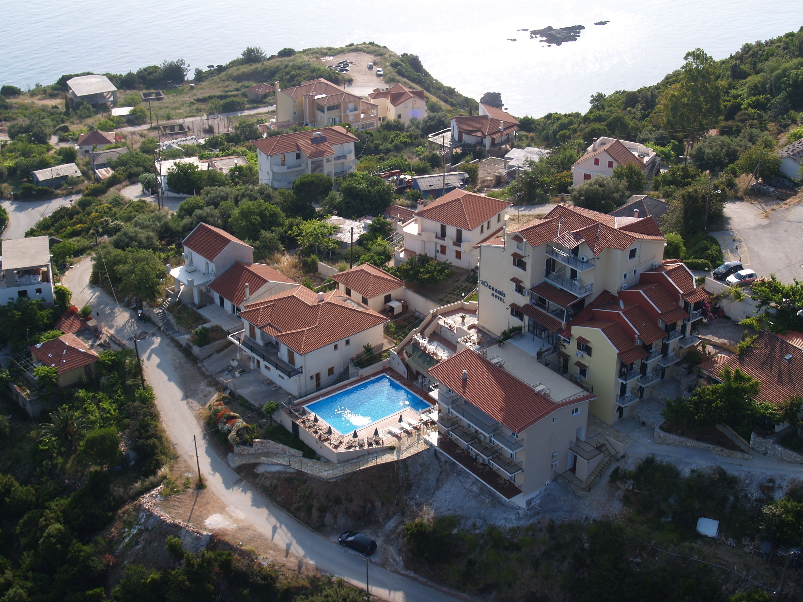 Vista aérea de um complexo hoteleiro costeiro com vários edifícios, piscina e estacionamento.
