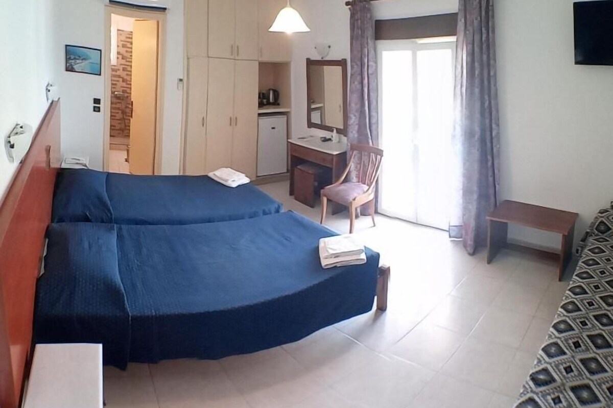Ein Hotelzimmer mit zwei Betten, einem Schreibtisch, einem Stuhl, einem Fernseher und einem sichtbaren Badezimmer durch eine offene Tür.