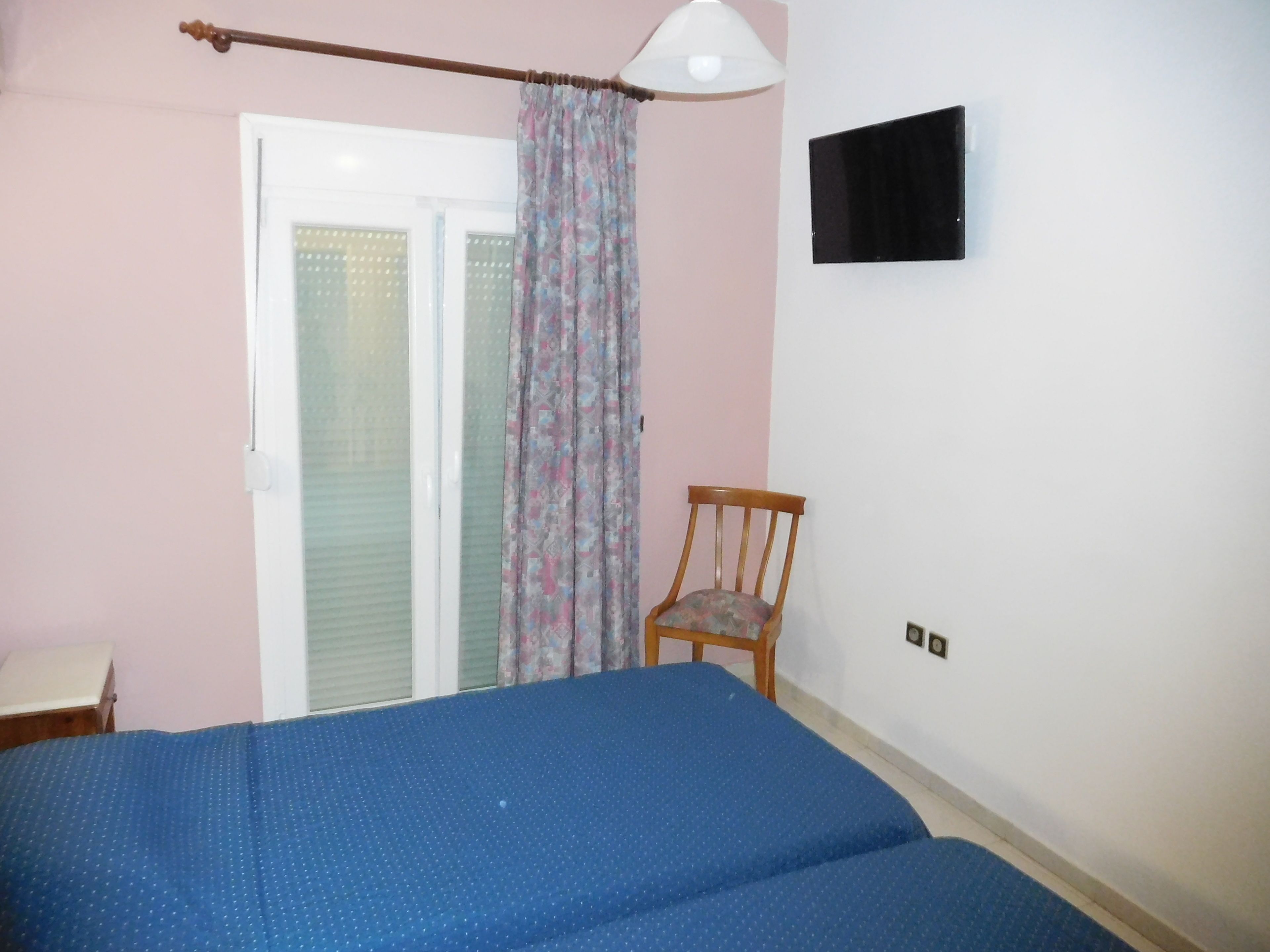 Un dormitorio con cama, una silla, televisor y ventana con cortinas.