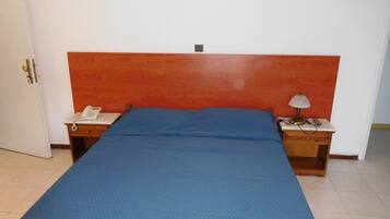 Habitación individual con una cama y cabecera roja, una mesita de noche con lámpara y teléfono.
