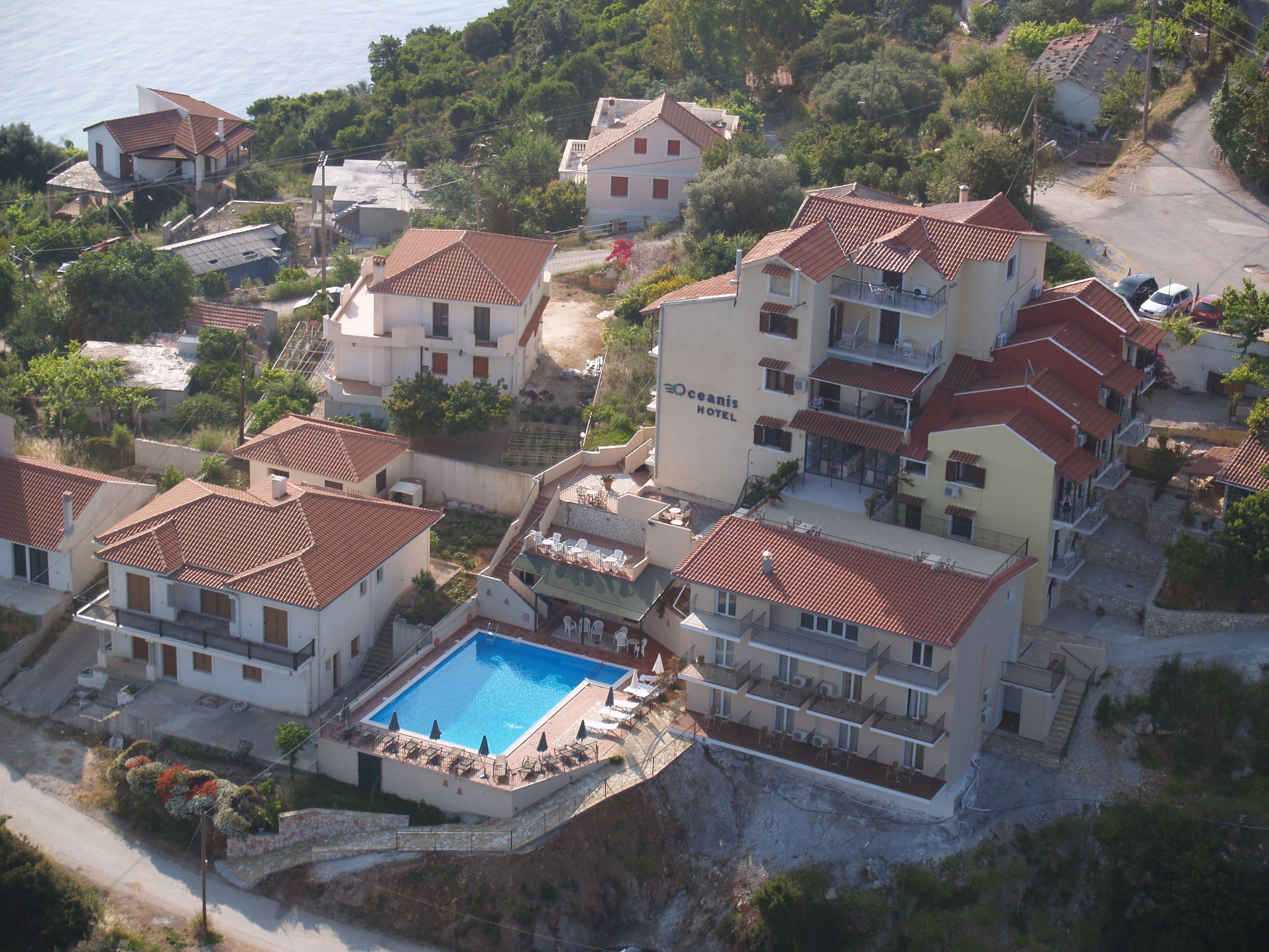 An aerial view of a coastal hotel with multiple buildings, a swimming pool, and a beach in the background.