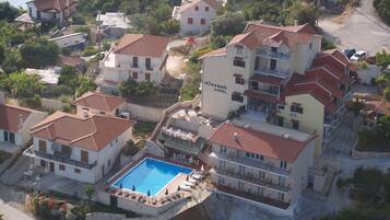 An aerial view of a coastal hotel with multiple buildings, a swimming pool, and a beach in the background.