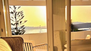 A hotel room with a bed, a chair, and a view of a tree and mountains through a glass door. - Afrodite Boutique Hotel (Paros)