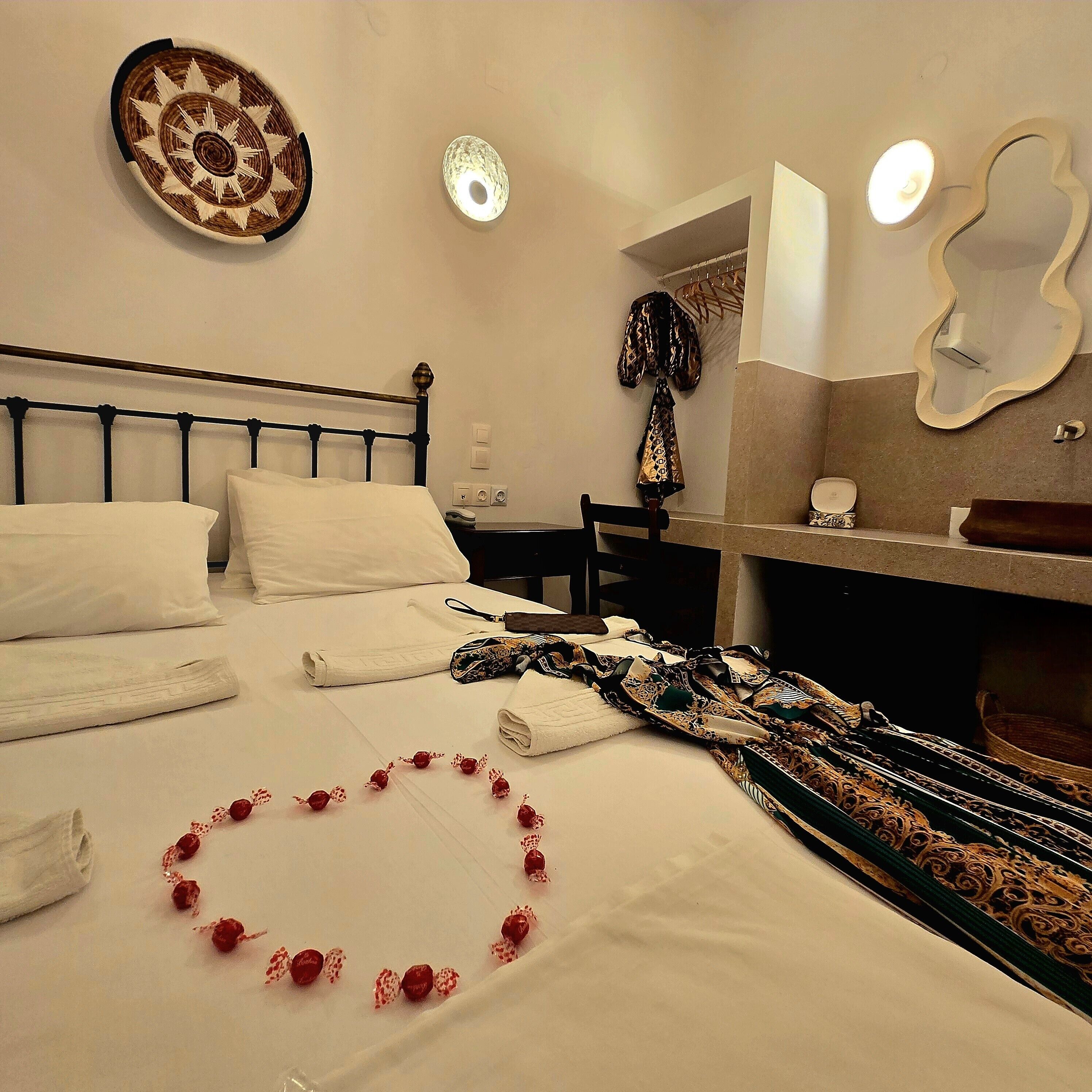 A neatly made bed with white linens, a decorative wall hanging, and a bathroom with a mirror and towel rack.