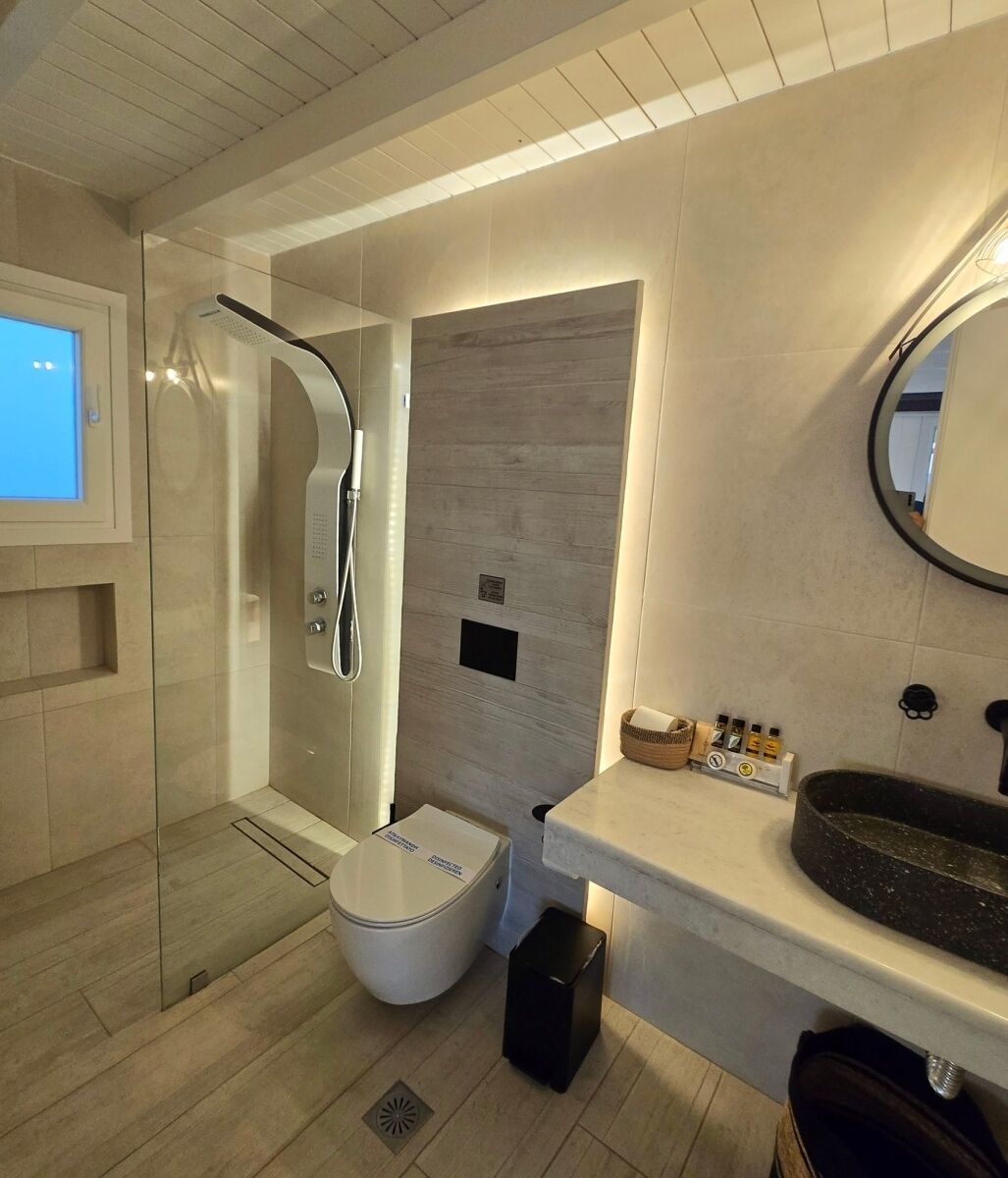 A modern bathroom with a glass-enclosed shower, a white toilet, a vanity with a black sink, and a mirror.