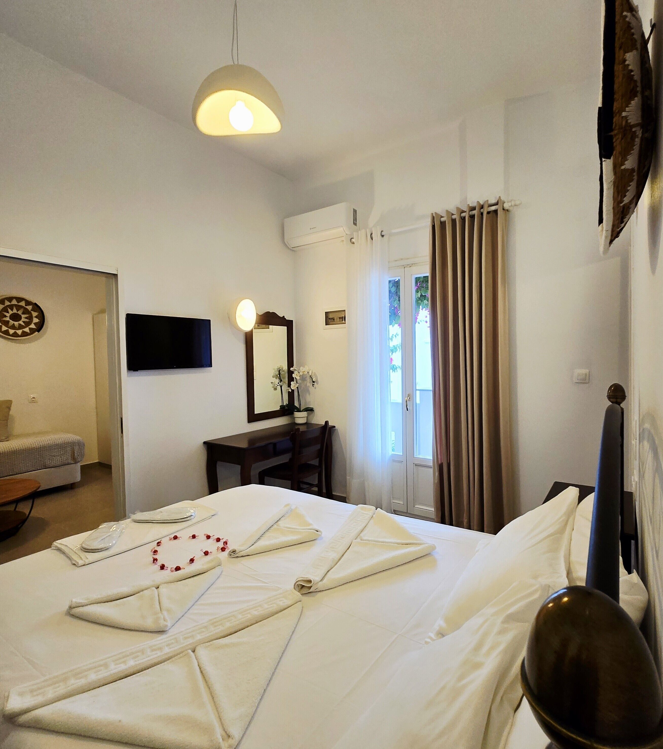 A hotel room with a bed, a desk, a chair, a television, a mirror, and a window with curtains.
