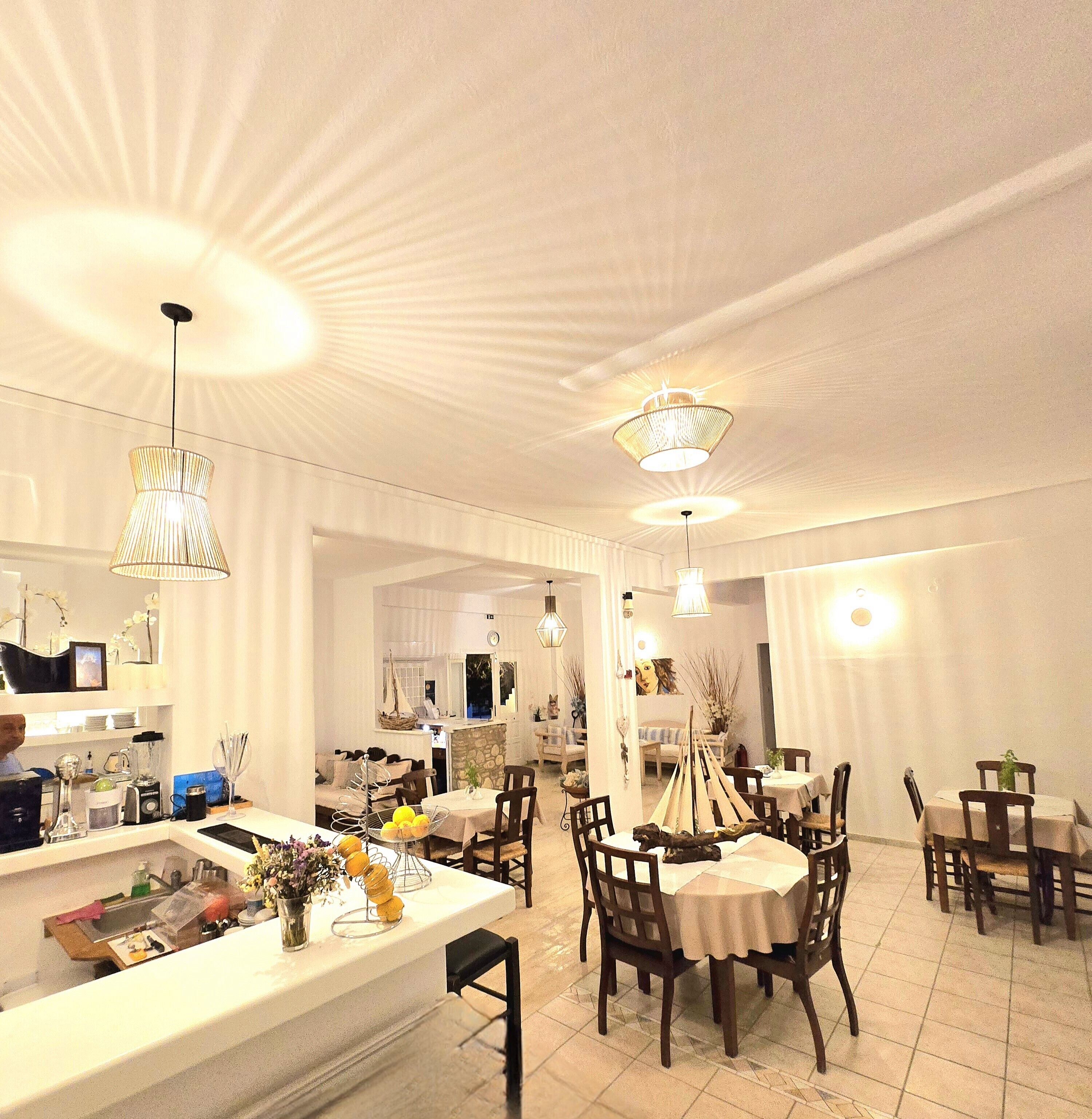 A spacious dining area with multiple tables and chairs, a central island with a sink and various items, and pendant lighting.