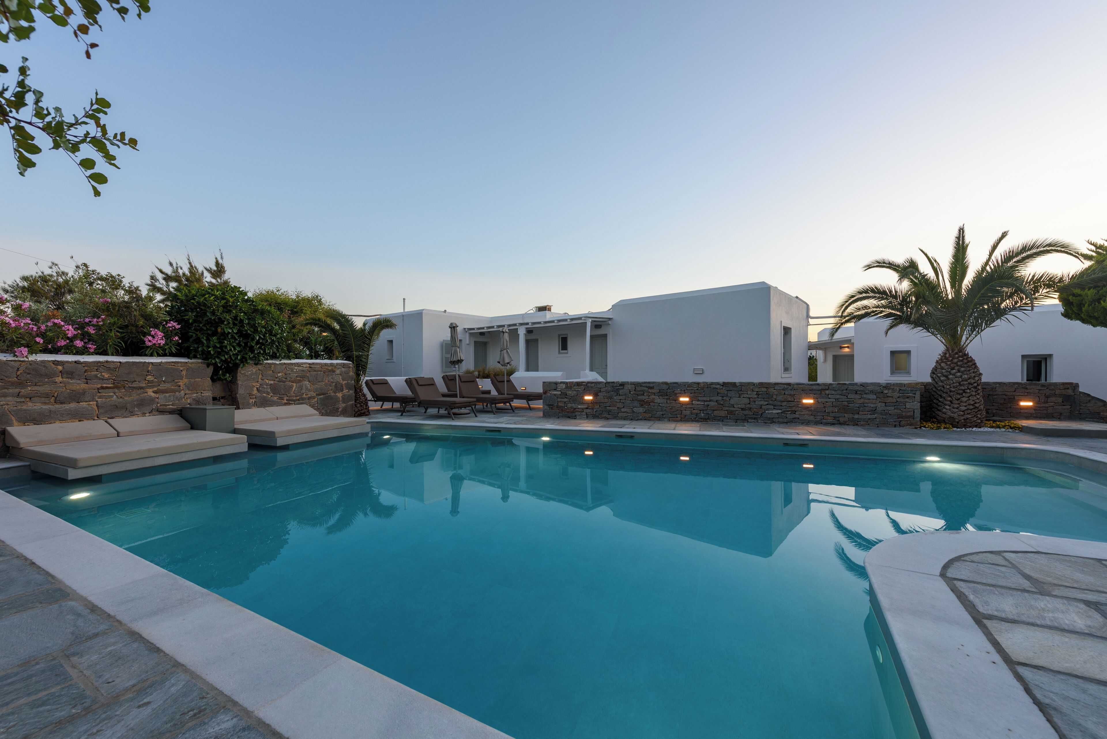 Una piscina con sillas de descanso, un muro de piedra y un edificio blanco con tejado de piedra.