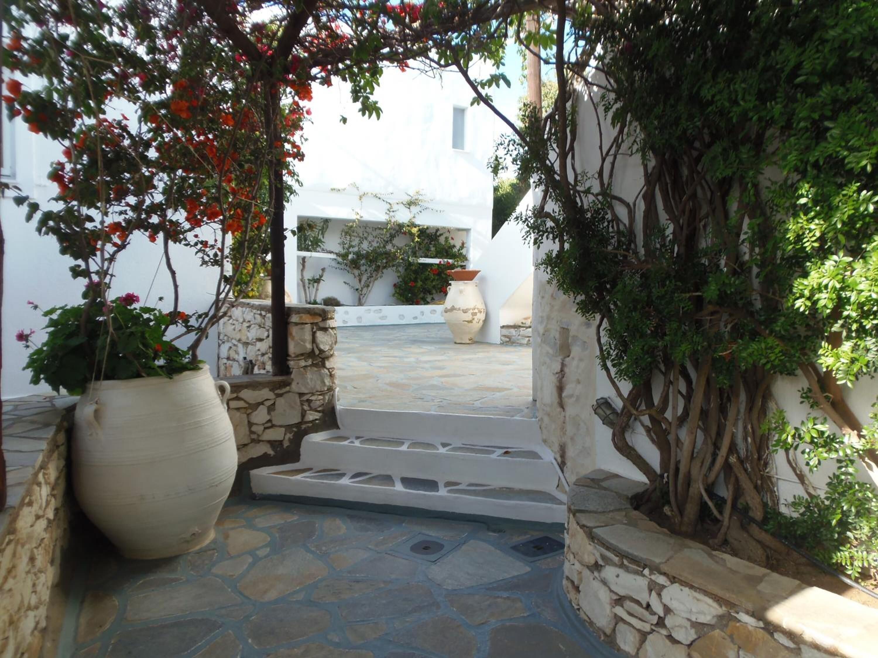 A stone pathway leading to a white building with a garden area featuring potted plants and a large vase.