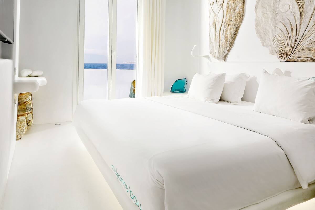 Une chambre d’hôtel moderne avec un grand lit, une vue sur la mer et un mur en pierre.