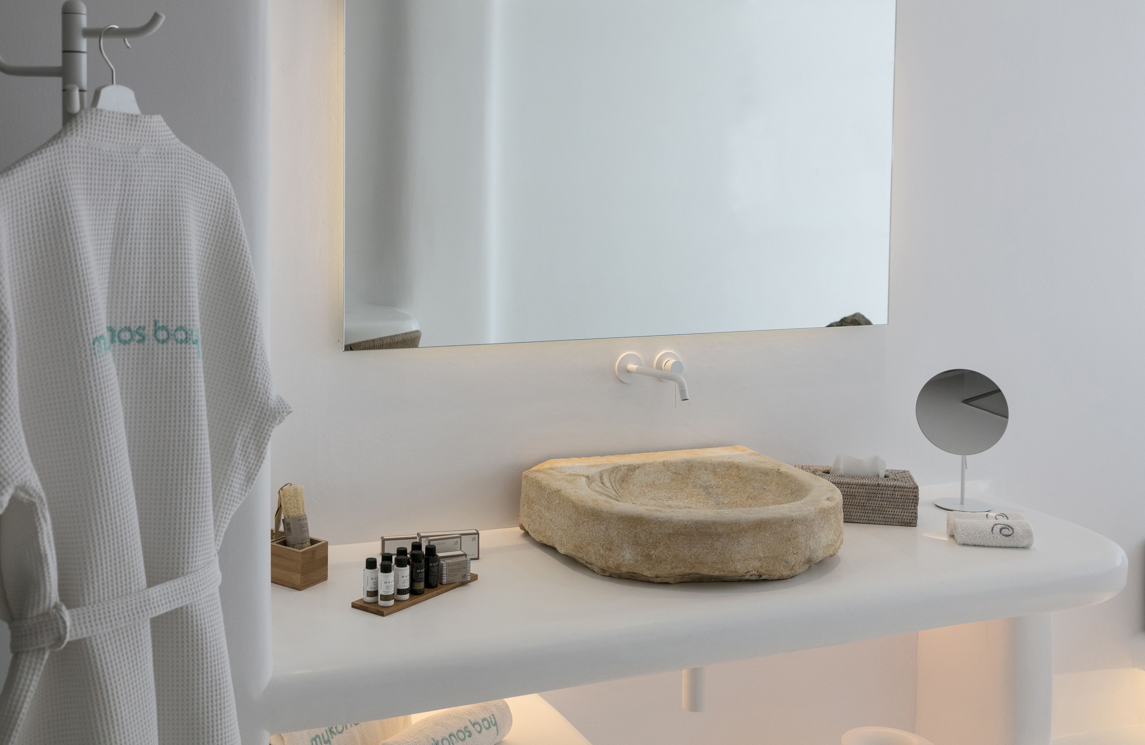 A modern bathroom with a white sink, a round mirror, and a towel rack.