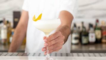 Une personne tenant un verre à martini, décoré d’une feuille jaune, dans un bar où l’on aperçoit des bouteilles en arrière-plan.