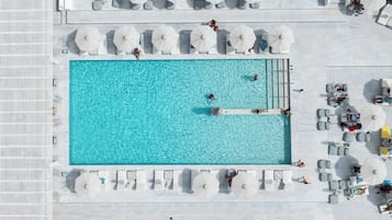 Una piscina en la azotea con varios niveles de asientos y zonas para tomar el sol, rodeada de sombrillas y sillones de descanso.