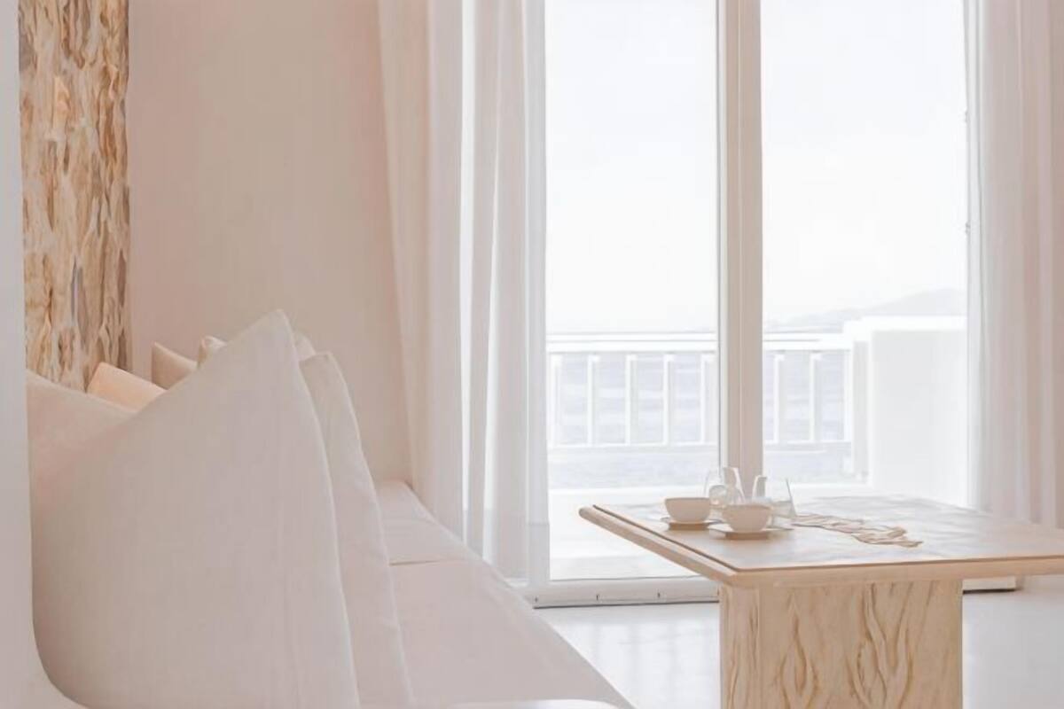 Une pièce avec un canapé blanc, une table en bois sur laquelle se trouvent une tasse et une soucoupe, et une vue sur un balcon.