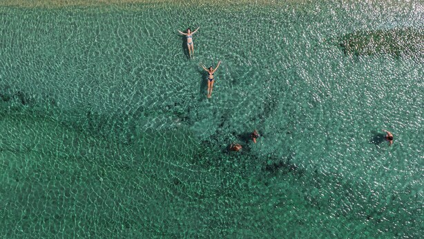 An aerial view of a beach with clear turquoise water, sun loungers, and umbrellas.