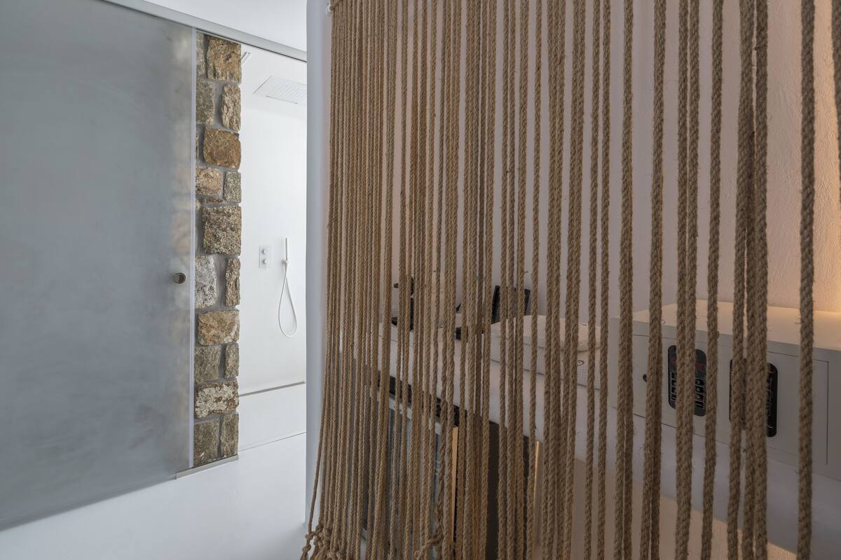 Une pièce avec un mur en pierre, une porte blanche et un rideau en corde.