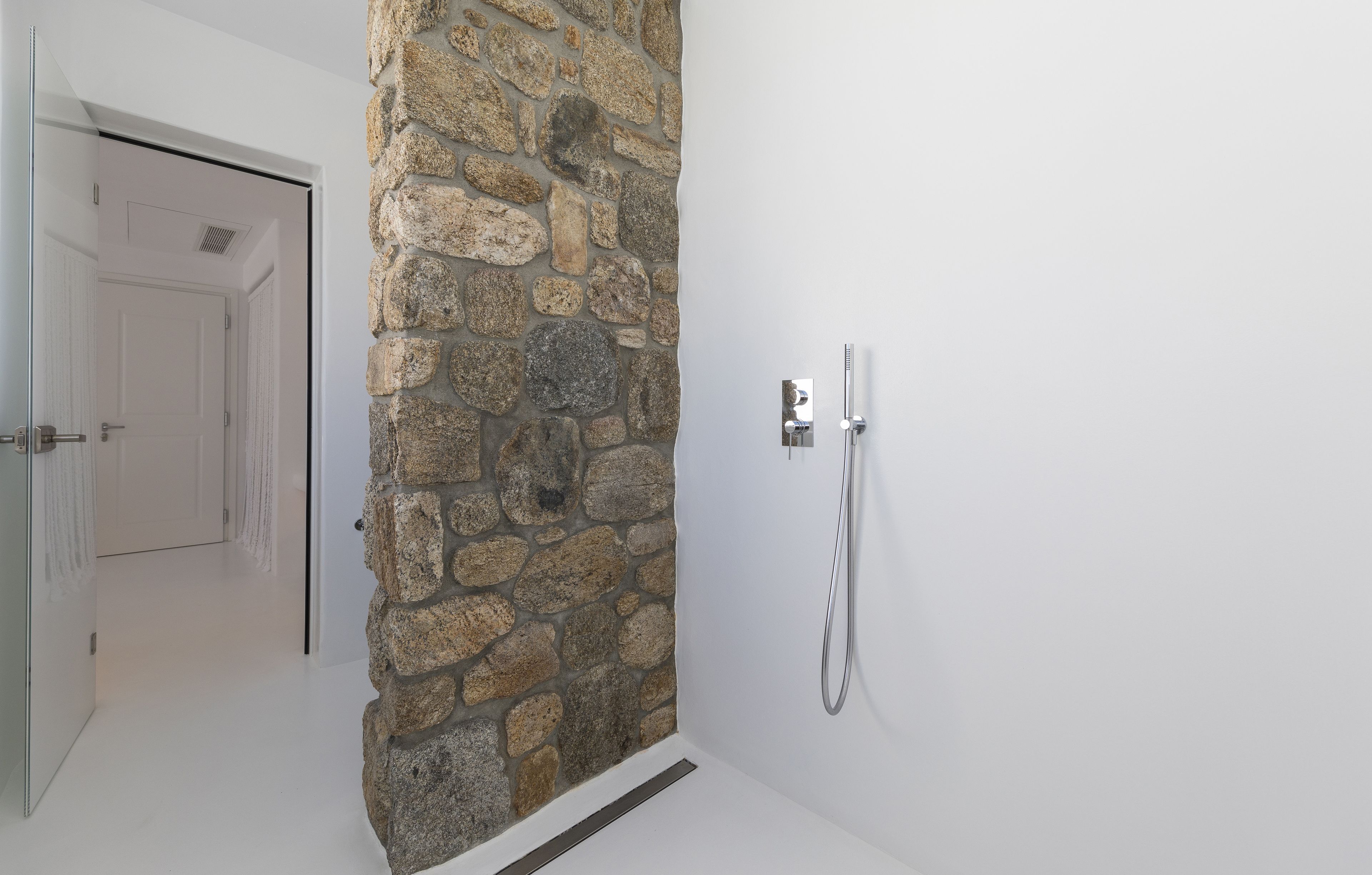 A bathroom with a stone wall, a shower, and a white door.
