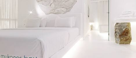 A modern hotel room with a large bed, a stone accent piece, and a view of the hallway.