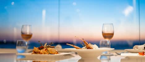Una mesa servida con platos de comida y copas de vino, con una vista del cielo al fondo.