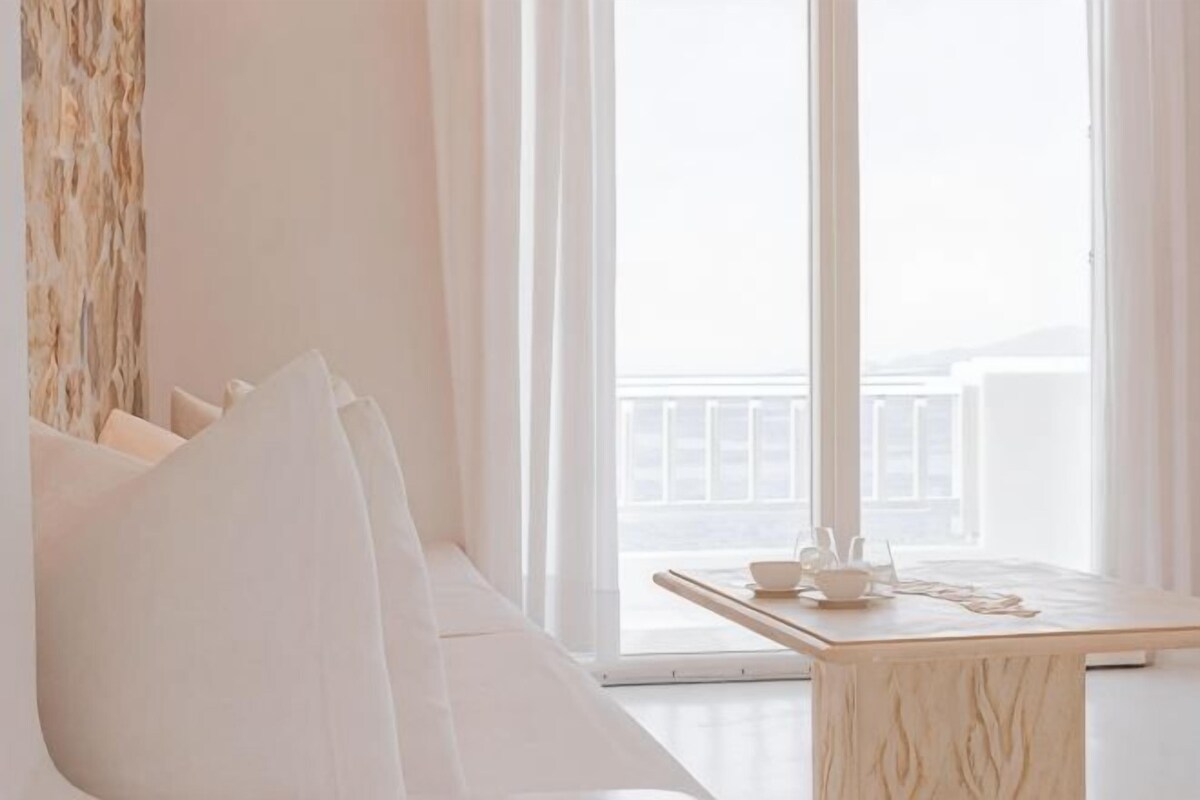 A room with a white sofa, a wooden table with a cup and saucer, and a view of a balcony.