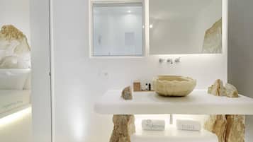 A modern bathroom with a white sink, a mirror, and a window with blinds.
