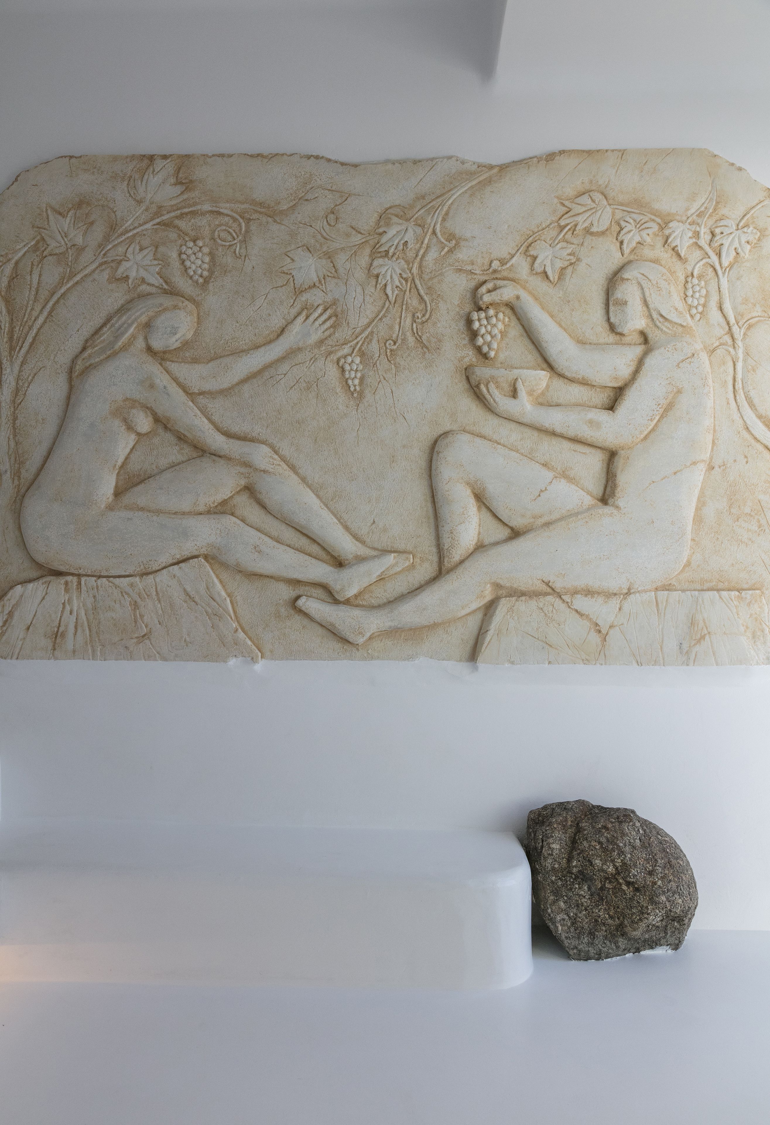 A relief sculpture of two figures, one holding grapes and the other reclining, with a rock beside it.