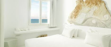 Un dormitorio con una cama grande, vista al mar a través de una ventana y un cabecero decorativo.