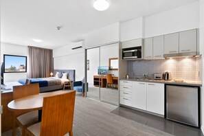 Ett modernt hotellrum med en säng, ett skrivbord, en stol, en matplats och ett litet kök.