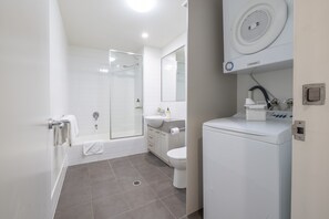 Ein modernes Badezimmer mit einer einbruchsicheren Duschkabine, einem weißen Waschbecken und einer integrierten Waschmaschine.