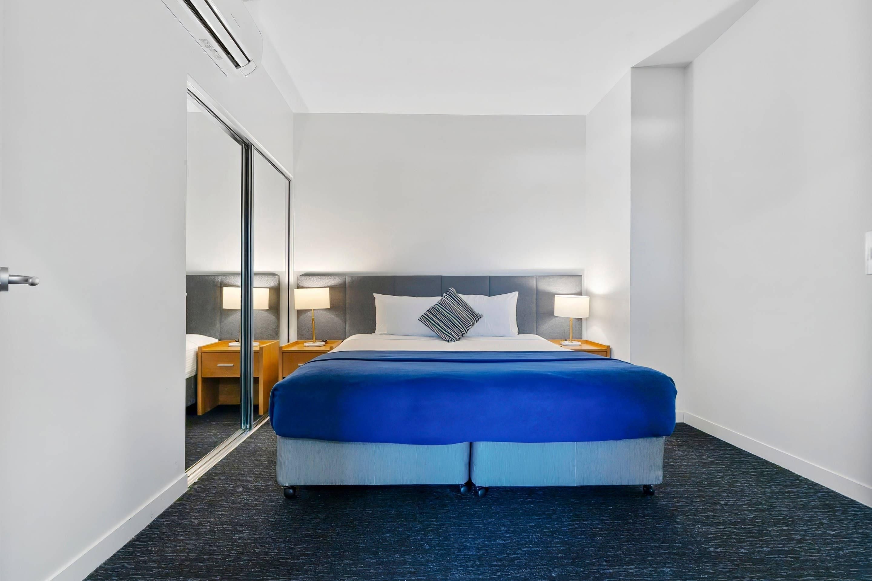 Une chambre d’hôtel avec un grand lit, une tête de lit, des tables de chevet, des lampes et un miroir.