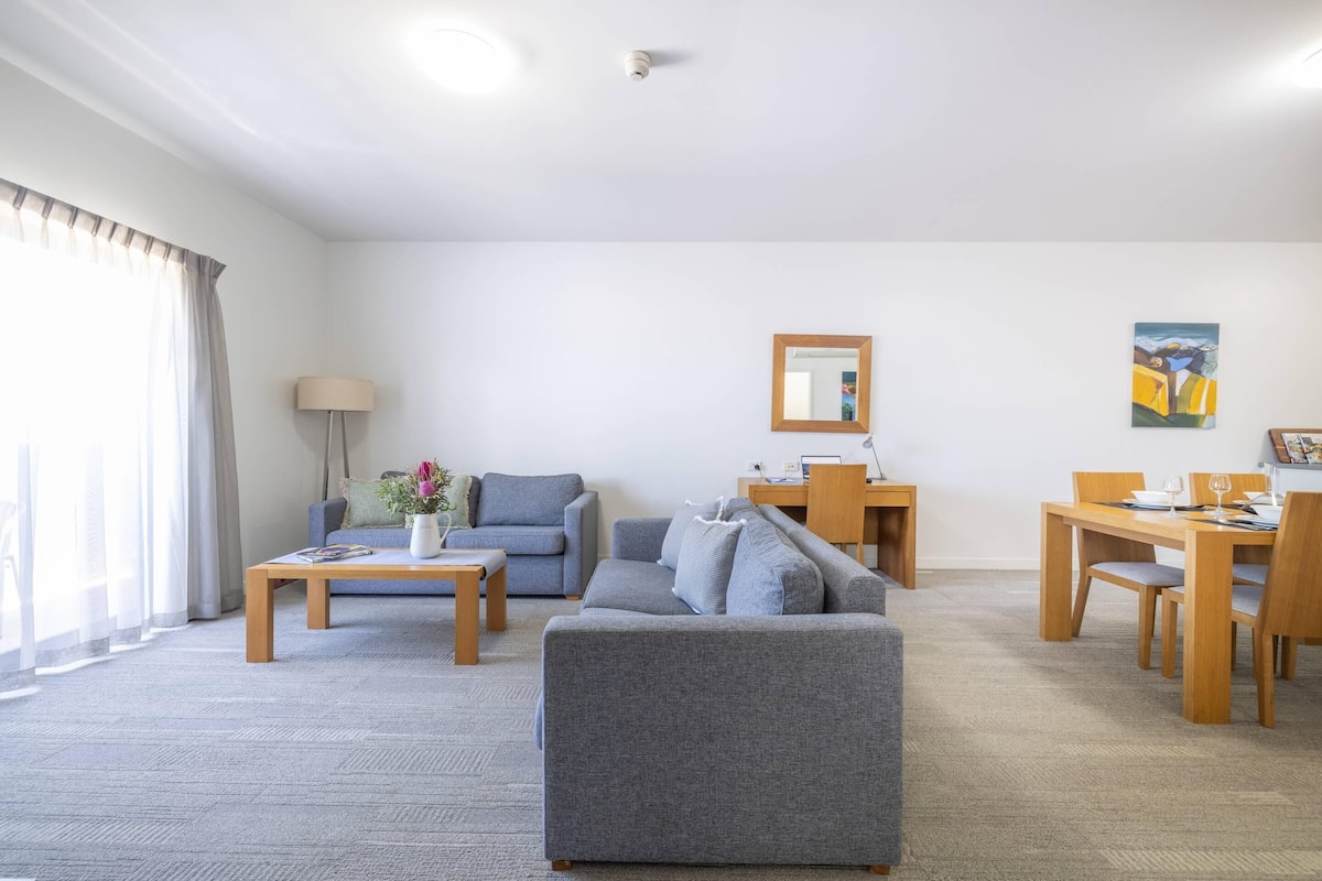 A modern living room with a grey sofa, a wooden coffee table, and a dining area with a wooden table and chairs.