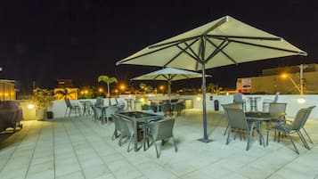 An outdoor patio with tables and chairs, a large umbrella, and a barbecue grill.