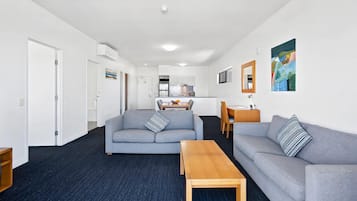 A modern living room with two grey sofas, a wooden coffee table, and a kitchen in the background.