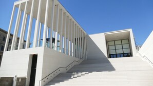 Un edificio moderno con fachada blanca, una escalera que conduce a un nivel superior y un cielo azul claro.